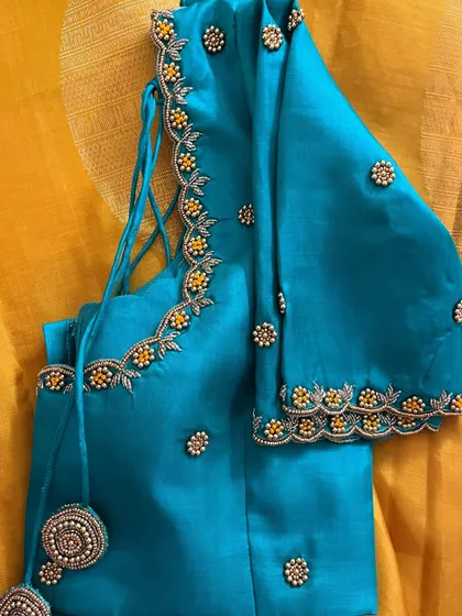 A full view of the simple and elegant teal blouse. The delicate beadwork on the neckline and sleeves, along with the matching tassels, makes it a beautiful choice for any festive occasion.
