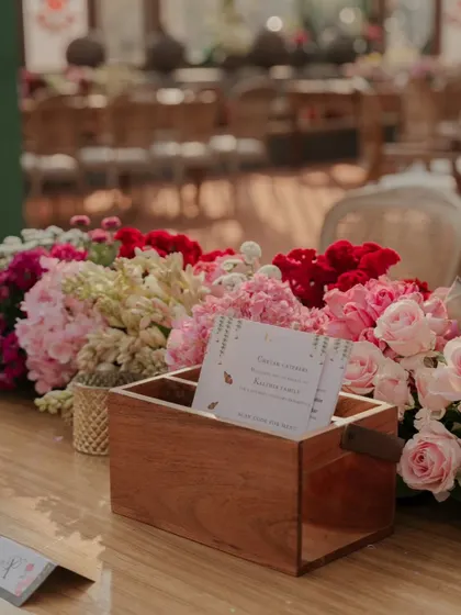 A custom wooden box for guest messages, surrounded by a lush arrangement of pink and red flowers. I love creating interactive and personalized elements for guests.