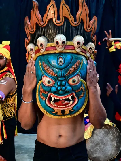 A blue evil eye warder mask from Nepal, held by a traditional Dollu Kunitha dancer. These masks are believed to protect against malicious forces, making them a vibrant and culturally rich element for any entrance.