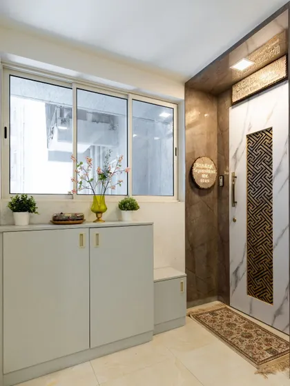 A bright and practical foyer design with a marble-and-gold-patterned door, a sleek shoe cabinet, and a small bench for seating.