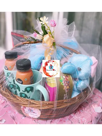 A charming gift basket for a family, featuring adorable elephant-themed mugs, a blue plush toy, and bottled drinks, all neatly wrapped in white tulle. It's a sweet gift for a family with young children.
