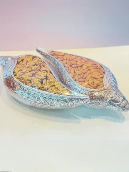 For a truly regal touch, I offer dry fruits presented in these intricately carved, silver-plated shankh (conch) shaped containers. This image shows walnuts and almonds, sealed for freshness.