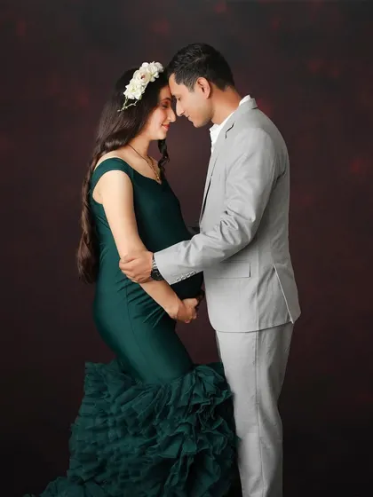 An intimate couple's portrait against a rich, textured backdrop. The deep green of the gown and the floral hairpiece add a touch of earthy elegance to this maternity photo.