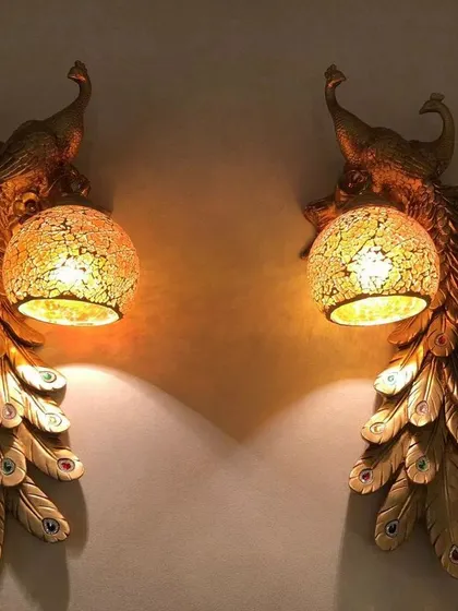 Inspired by India's national bird, these peacock wall lights bring a touch of regal artistry to your home. The detailed golden feathers and cracked glass globe create a warm, inviting glow that is both dramatic and elegant.