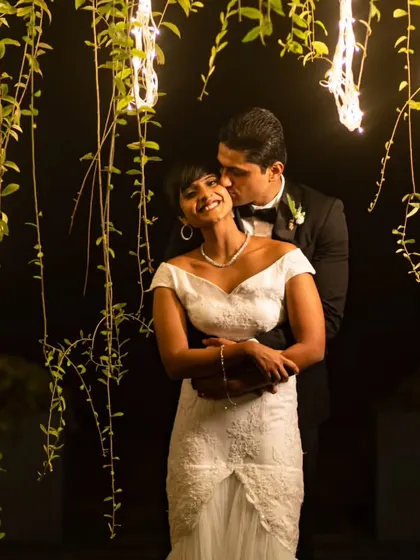 A beautiful moment between a newly married couple, framed by hanging greenery and soft lights during their evening reception.