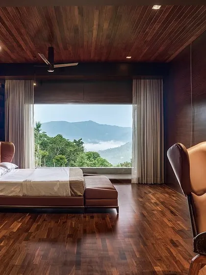 The master bedroom in the Chikmagalur residence, where a feature wall of stacked wooden blocks adds texture and warmth. A large window frames the mountain view, making it the primary artwork in the room.