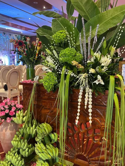 An artful arrangement combining fresh flowers, tropical foliage, and traditional fruit offerings for a rich and textured look.
