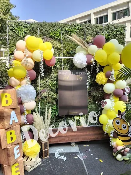 A full view of an outdoor "What will it Bee?" gender reveal party. I used a green wall as a natural backdrop, adding wooden 'BABEE' blocks, a cute bee cutout, and a balloon garland in yellow, maroon, and beige.