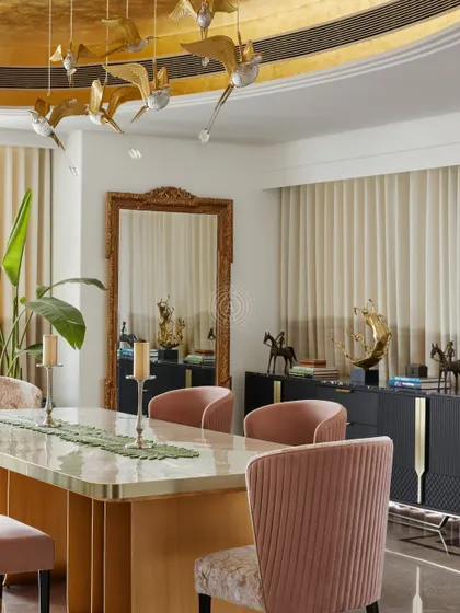 The dining area is filled with luxurious details, from the gold-leaf ceiling to the large ornate mirror and sculptural accessories on the sideboard. The space is designed to feel grand and opulent.