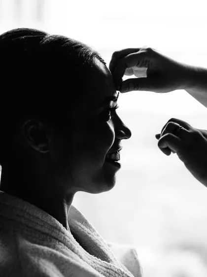 A silhouette of the bride, Amrutha, getting her makeup done. This black and white shot focuses on the form and the action, creating an artistic and timeless image of the getting ready process.