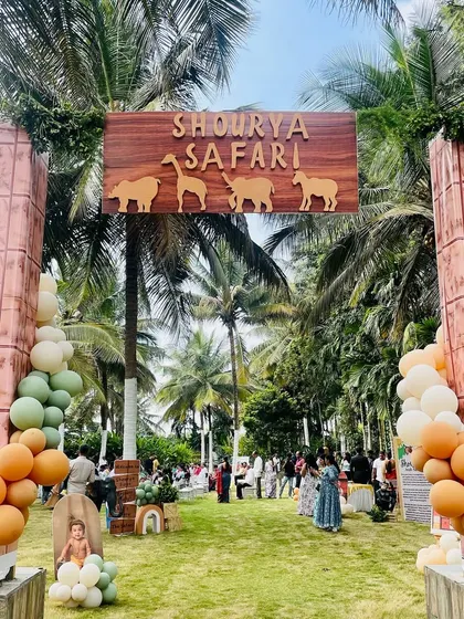A stylish and modern entrance for Shourya's safari party. The setup features a wooden sign with animal silhouettes, set between two pillars and framed by organic balloon arches in muted orange, green, and white tones.