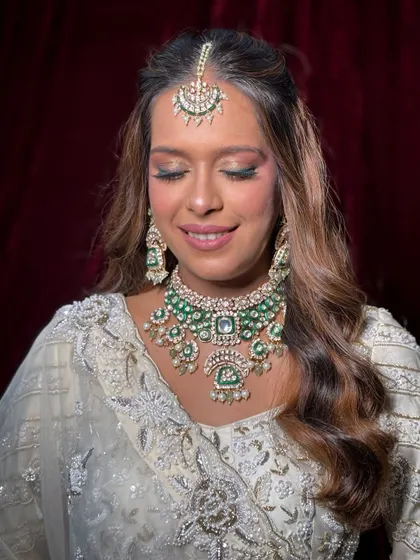 A beautiful bride in an elegant white embroidered lehenga, featuring a soft smokey eye with a hint of green to match her jewelry.
