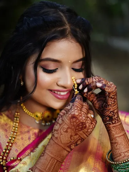 A candid moment capturing the final touches on a radiant Maharashtrian bride. This look features glowing skin, soft gold shimmer on the eyes, and traditional details like the nath, embodying grace and elegance.