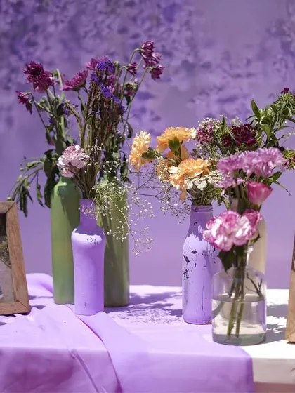 Another view of the memory station, showcasing the couple's photos in rustic wooden frames, alongside hand-painted bottles and fresh flowers, all in the event's soft pastel color scheme.