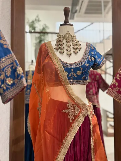 A close-up of a stunning lehenga set. The deep blue blouse with intricate floral embroidery is paired with a vibrant orange dupatta, a classic color combination that is always a winner.