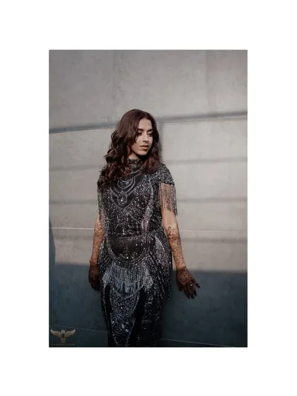 A striking portrait of the bride-to-be in a glamorous, fringed dress. The play of light and shadow highlights the intricate details of her outfit and her confident presence.