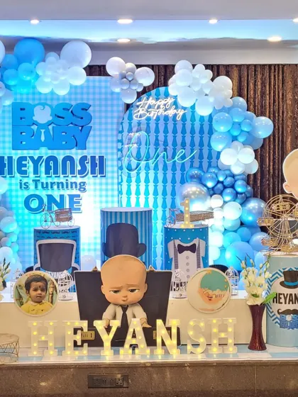 A fun and stylish Boss Baby themed birthday stage. The setup includes a custom light-up backdrop, character cutouts, themed pedestals for the cake, and marquee letters spelling out the birthday boy's name.