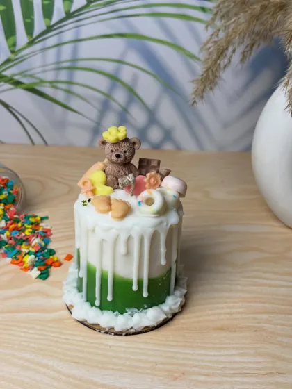 A close-up shot of my signature teddy bear cake candle. The green base, white drip effect, and adorable toppings make it a whimsical and sweet centerpiece or gift for any baby shower.