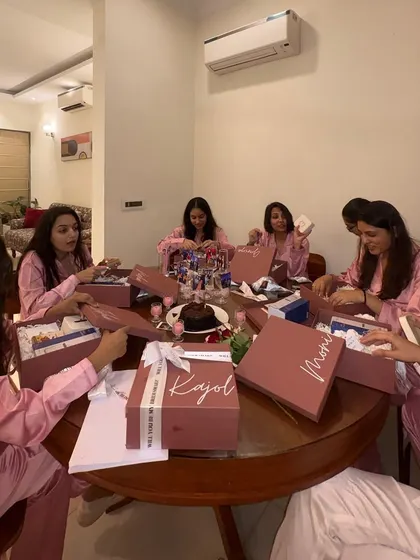 The unboxing begins. This candid shot captures the excitement as the bridesmaids open their personalized hampers together around the table.