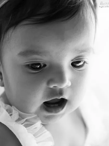 A close-up of a baby's curious expression. Black and white photography highlights the beautiful details, from her bright eyes to her tiny mouth.