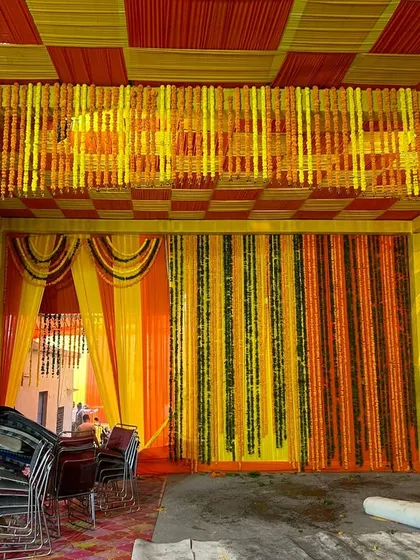 A full view of a pandal we set up for a home wedding. The ceiling features a checkered pattern of yellow and orange fabric, with dense marigold hangings creating a rich, traditional look.