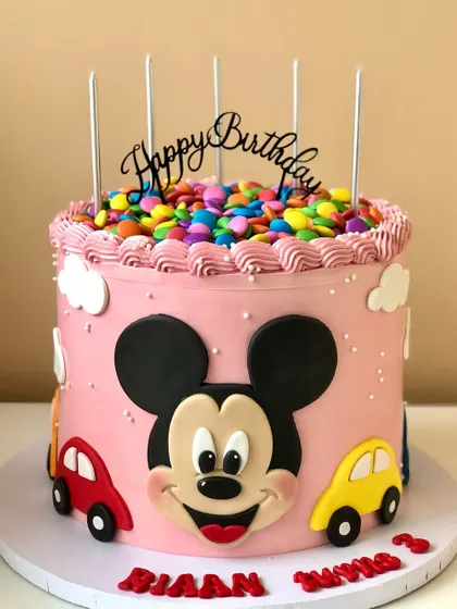 A happy and colorful Mickey Mouse cake, topped with a pile of gems for an extra touch of fun. The bright pink buttercream makes it a joyful centerpiece.