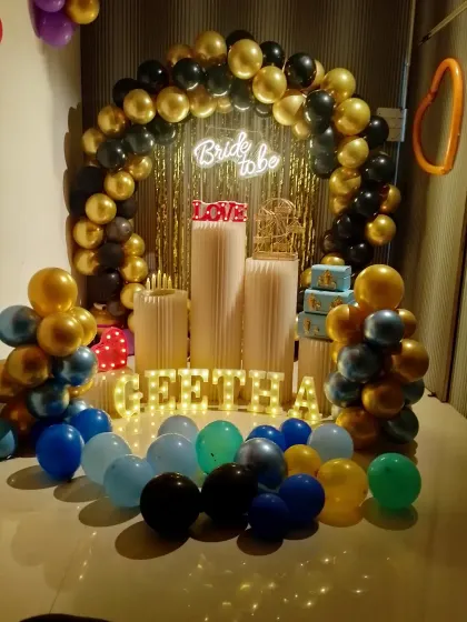 A chic 'Bride to be' setup for a pre-wedding celebration. The black and gold balloon arch, neon sign, and personalized light-up letters for 'GEETHA' make the bride-to-be feel truly special.