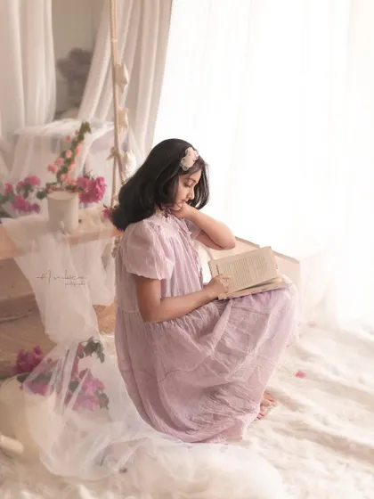 A dreamy, romantic portrait of a young girl reading in a soft, light-filled setting. This image tells a story, capturing the quiet magic of childhood imagination.