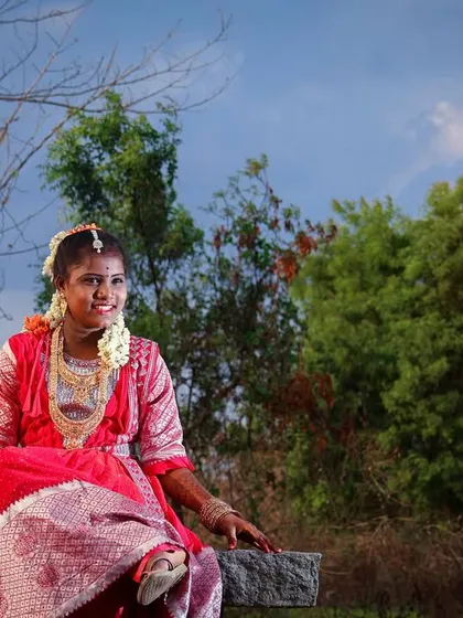 A relaxed outdoor portrait. The subject is seated on a stone bench, with the warm evening sun creating a beautiful flare, adding a dreamy quality to this traditional puberty ceremony photo.