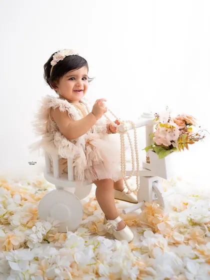 A happy baby girl on her tricycle, surrounded by a floor of white petals.
