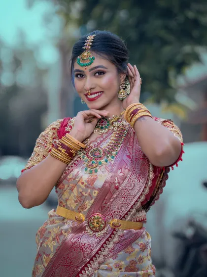 A smiling bride wearing a multi-layered haram with green stones and a matching maang tikka from our rental collection.