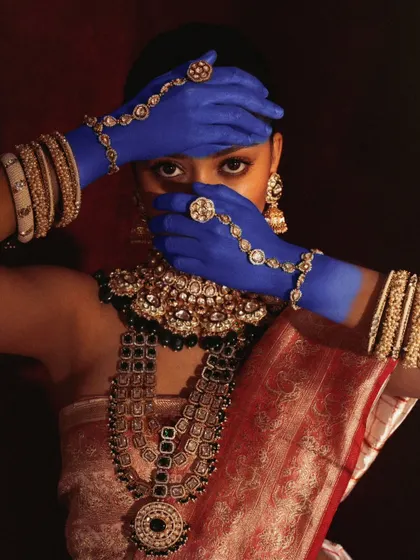 A powerful close-up where the model's painted hands frame their face, creating a sense of mystery and highlighting the intricate jewelry.