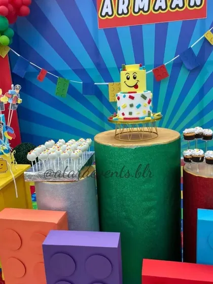 The dessert station is filled with treats, including a LEGO brick cake, cake pops, and cupcakes displayed on colorful, block-like stands.