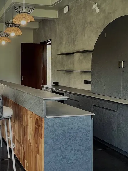 This bar area in a private club combines rustic and industrial elements. We used a concrete-finished bar front with a wooden inlay, woven bar stools, and exposed concrete walls, complemented by a custom arched cabinet for a touch of softness.