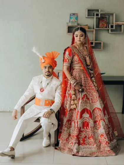 A modern royal portrait. The groom seated, the bride standing tall beside him, this pose creates a sense of partnership and regal elegance against a simple backdrop.