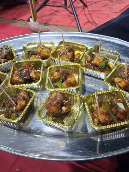 A tray of spicy Chili Paneer starters, served in individual gold foil cups with toothpicks for easy eating.