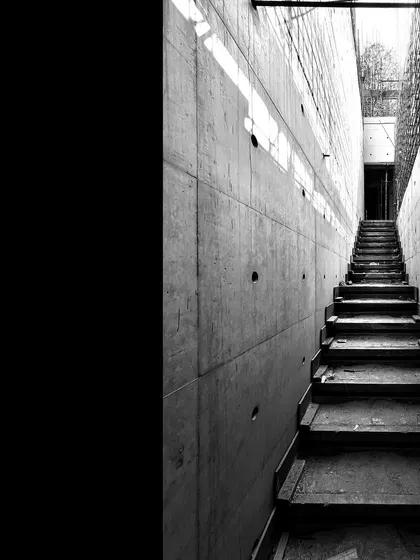 A narrow concrete staircase under construction. The image captures a dramatic perspective, with light filtering in from an opening at the top.