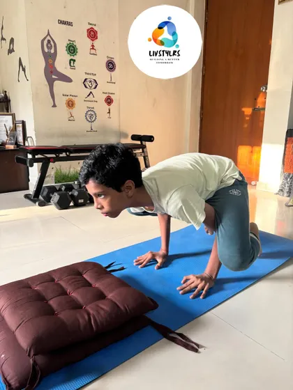 A young boy practices Bakasana (Crow Pose) with a cushion for safety. This arm balance builds incredible strength, confidence, and concentration.