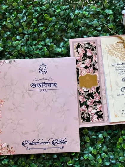 A beautiful Bengali wedding invitation in pastel pink with a floral design. The "Shubho Bibaho" text is elegantly printed on the cover.