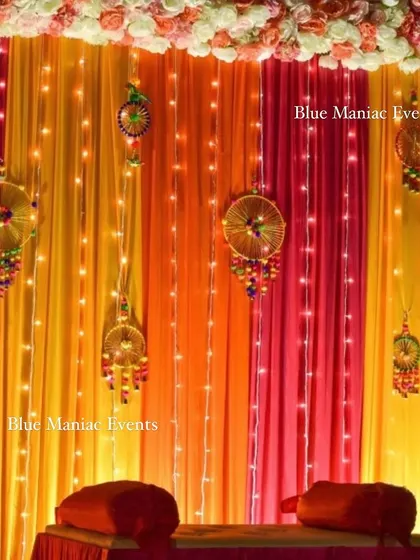 A close-up of the Mehendi night decoration on a home terrace, showing the warm lighting and traditional hangings against the colorful drapes.