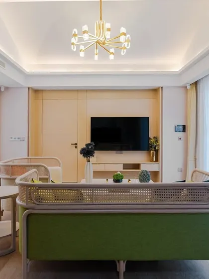 A minimalist living room design featuring a custom green and natural cane sofa. The light wood flooring and sheer white curtains create a bright, airy, and calming atmosphere.
