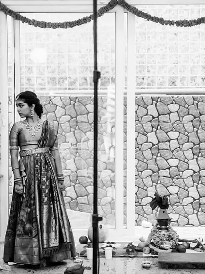 A behind the scenes, black and white shot of a young woman during a home ceremony. Including the lighting setup adds a raw, documentary feel to this quiet, preparatory moment.
