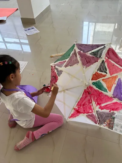 A close-up shot of a young artist concentrating on filling in the sections of her umbrella. This requires precision and patience, skills that we nurture through engaging art projects.