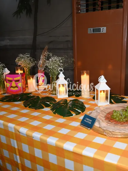 Rooted in nature, wrapped in detail. A tablescape from our tribal-themed celebration, featuring a checkered tablecloth, monstera leaves, and candle-lit lanterns.