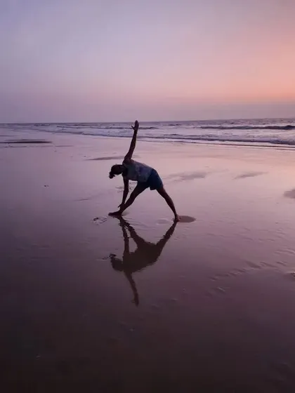 A student practices Trikonasana (Triangle Pose) on the beach. The silhouette against the twilight sky shows the beautiful lines and openness this pose creates.
