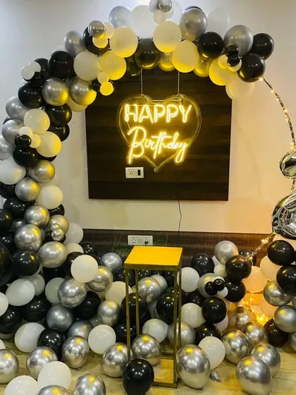 A 22nd birthday party with a black, white, and silver balloon arch and a heart-shaped neon sign.