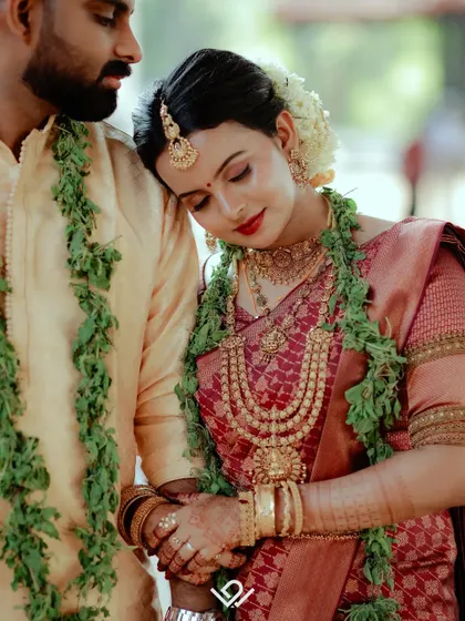 A tender moment where the bride rests her head on the groom's shoulder, both adorned in beautiful garlands.
