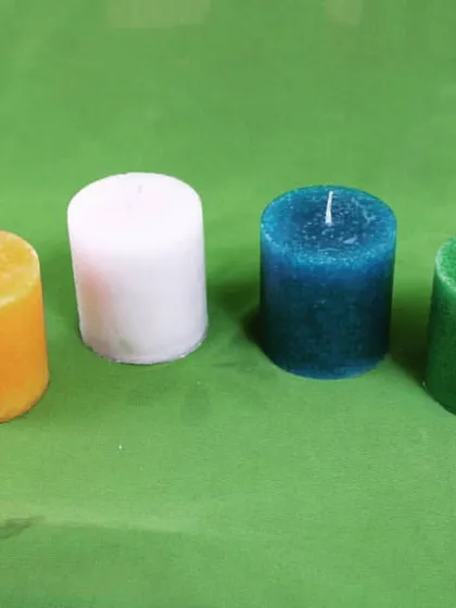 My small pillar candles in yellow, white, blue, and green, arranged on a green cloth. This shows the actual handmade product you will receive.