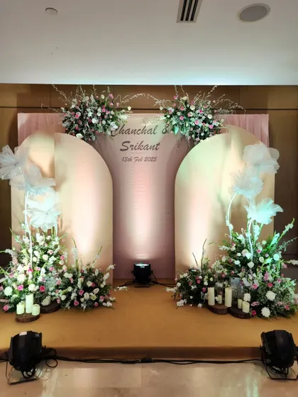 Soft, romantic, and elegant, this stage design uses blush-pink arched panels and delicate floral arrangements. The addition of whimsical white tulle bows and warm uplighting creates a fairytale setting for an engagement or reception.