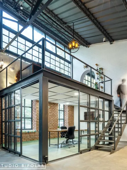 We inserted a glass-enclosed meeting room and a mezzanine level into the warehouse, adding functional space without sacrificing the open, airy feel. This "box within a box" concept maintains visual connectivity across the office.